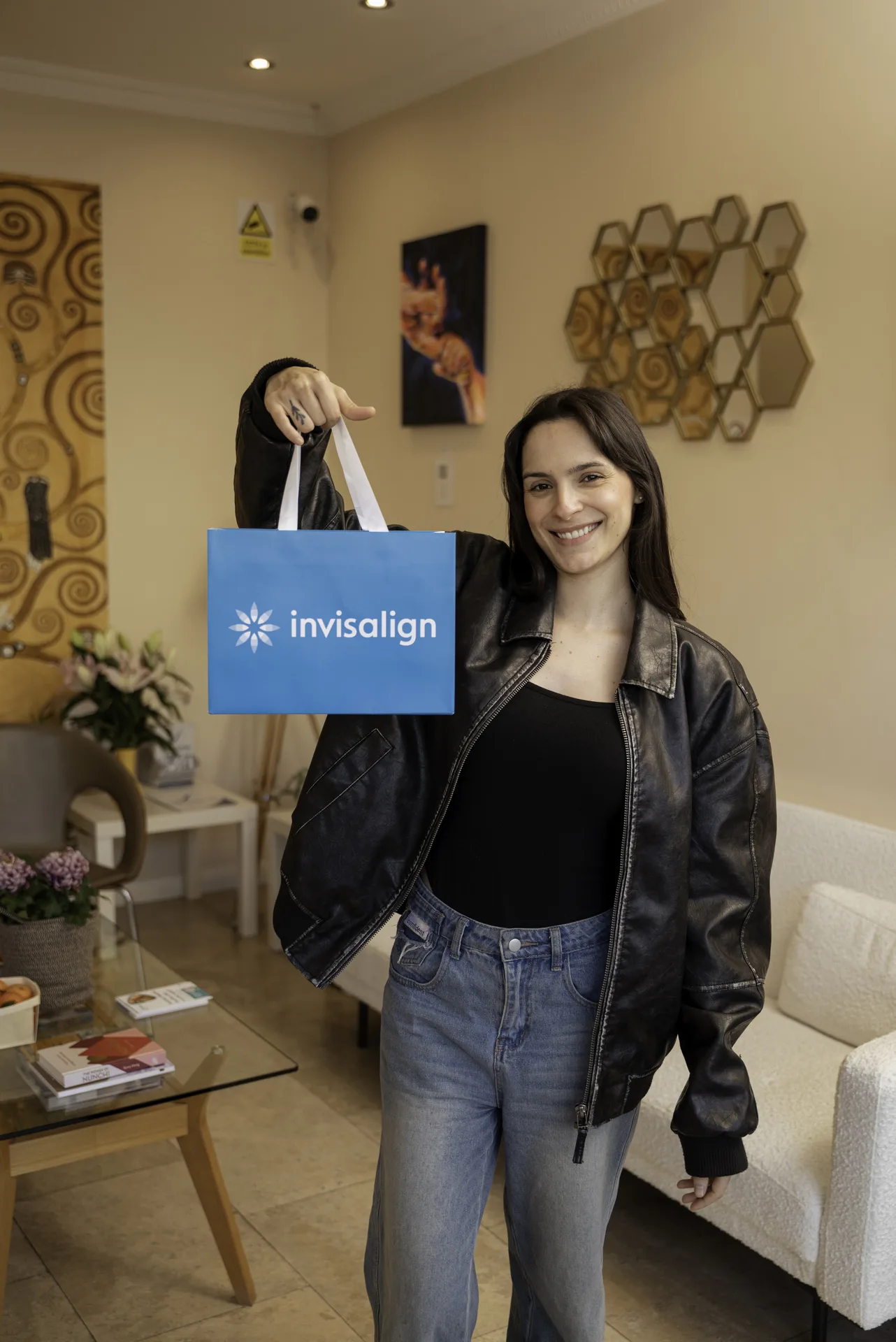 Smiling patient holding up an Invisalign bag in the clinic reception — Invisalign treatment time