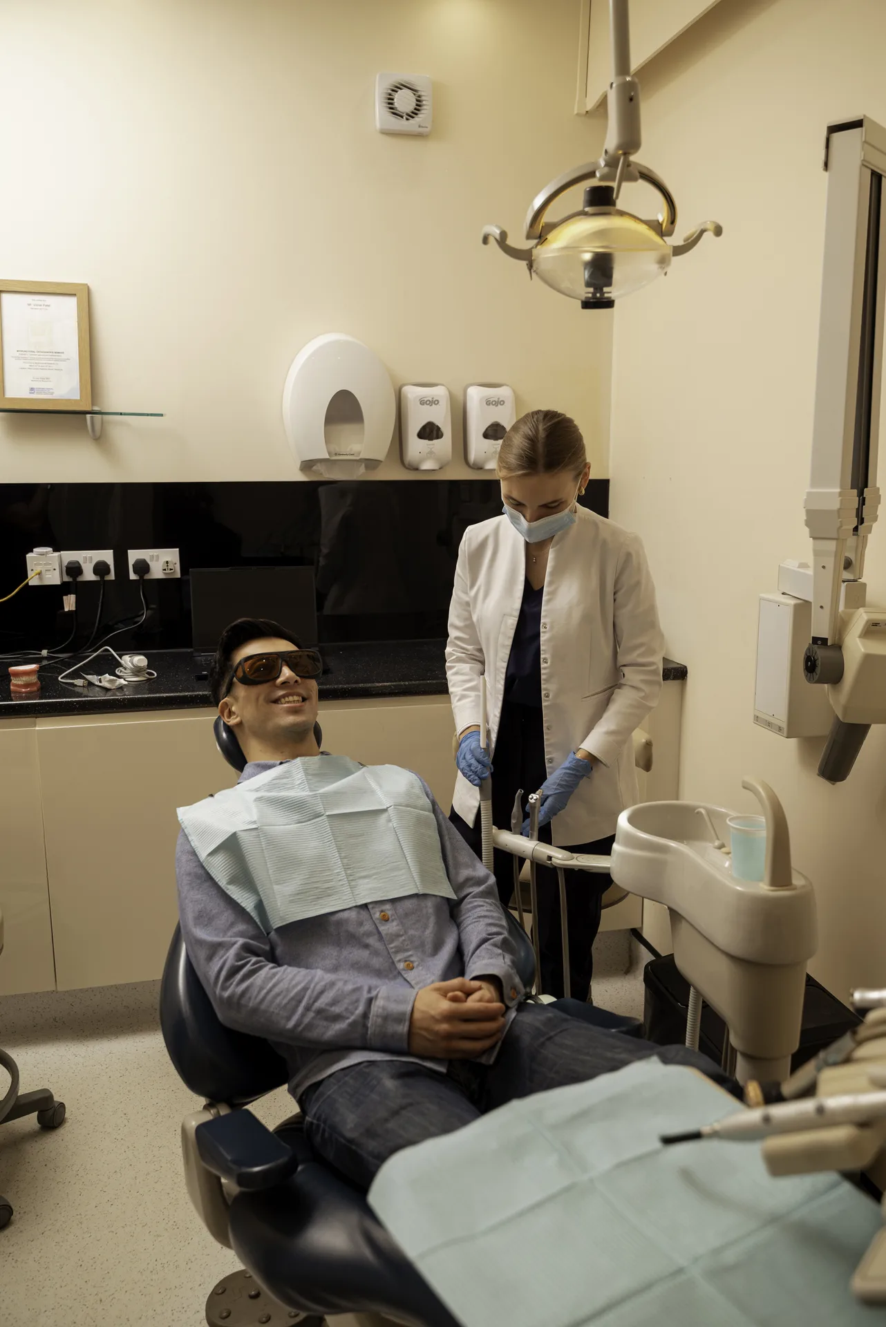 Patient in protective glasses reclining in the dental chair with a nurse beside him — root canal cost