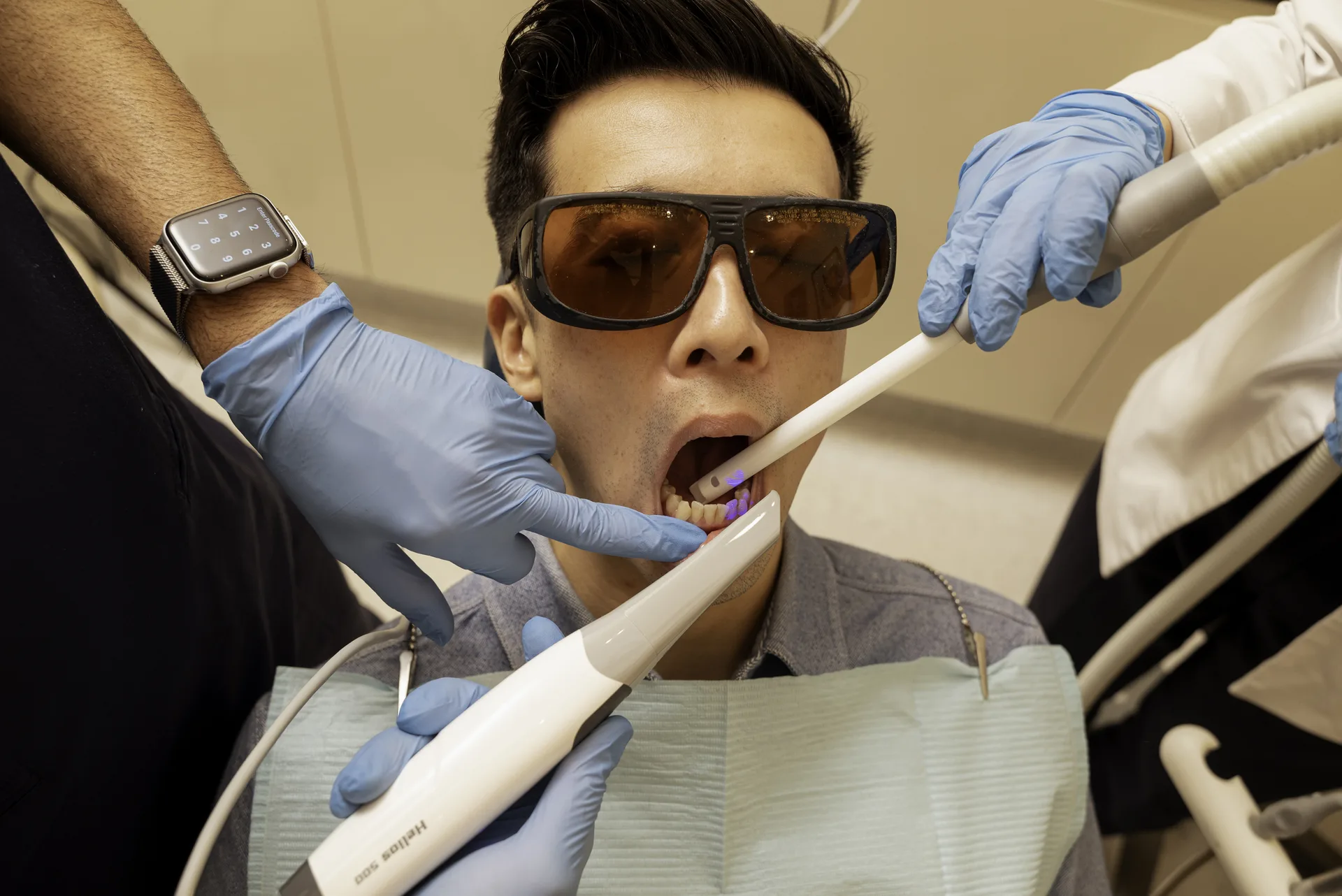 Emax vs porcelain veneers: patient in protective glasses receiving treatment with a curing light and suction
