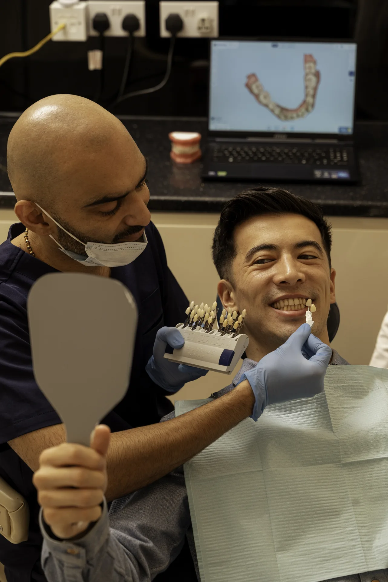 Dentist holding a shade guide to a smiling patient's teeth as he checks them in a mirror — composite bonding staining