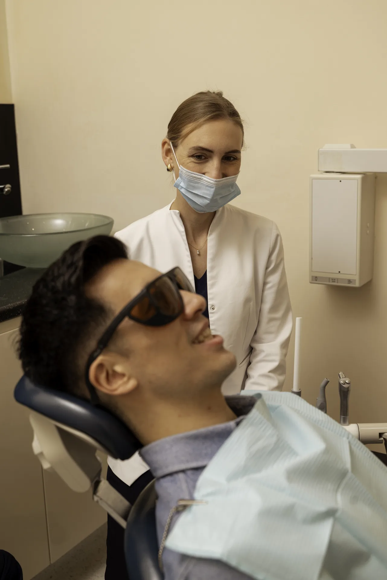 Patient in protective glasses reclining in the dental chair with a nurse behind him