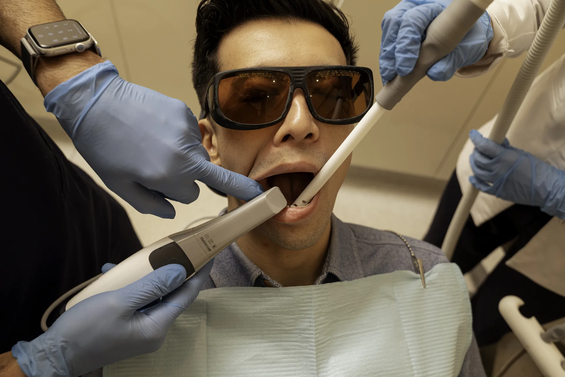 Emax veneers: patient in protective glasses having his teeth scanned and treated by the dental team