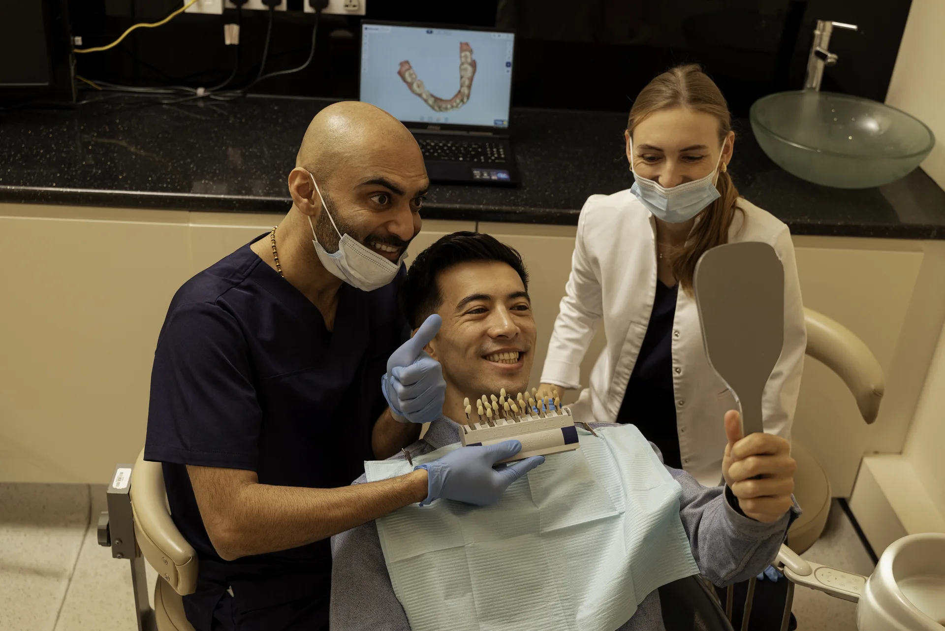 Veneers cost in the UK: dentist and nurse with a smiling patient holding a mirror and shade guide
