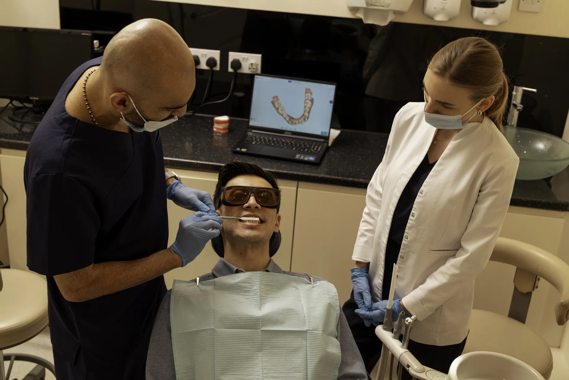 Invisalign effectiveness: dentist and nurse beside a smiling patient, with a digital scan of his teeth on a laptop