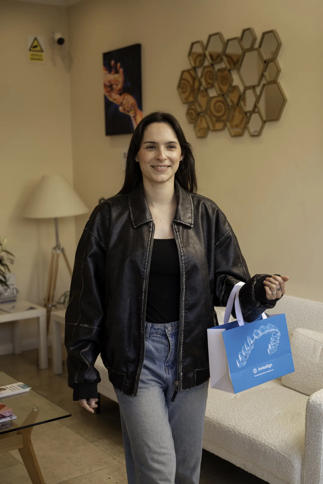 Smiling patient walking through the clinic reception with an Invisalign bag
