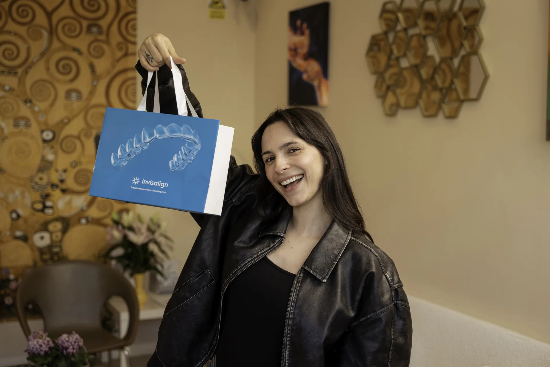 Invisalign Diamond provider: smiling patient holding up an Invisalign bag in the clinic lounge