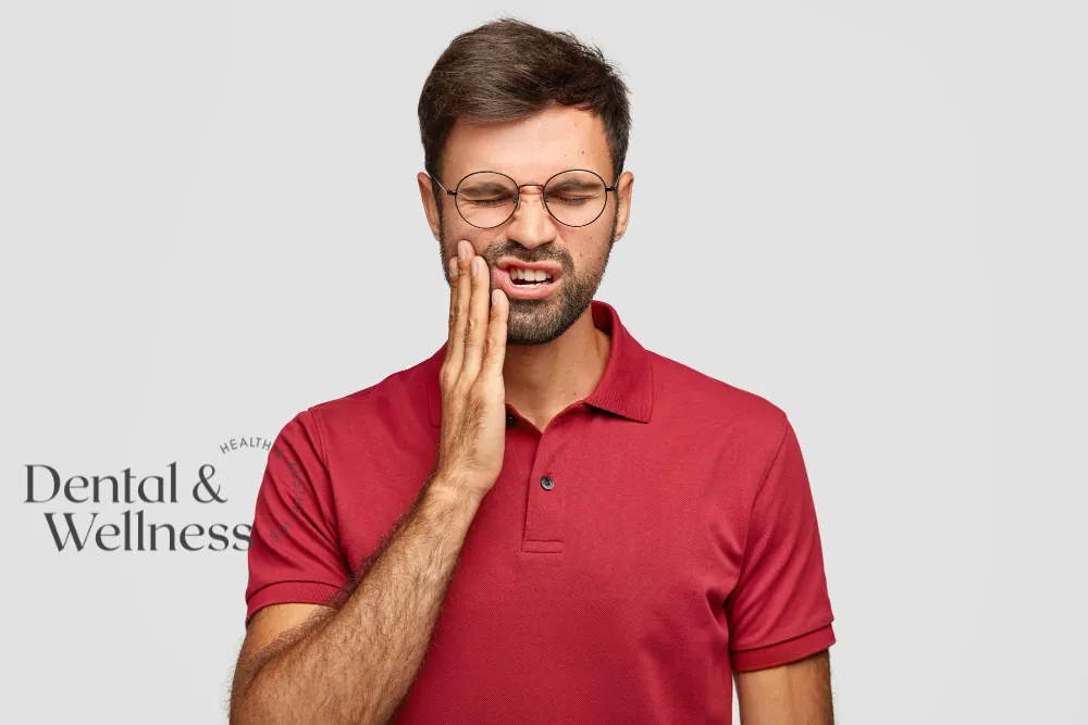 Emergency dentist: man in glasses wincing and holding his cheek with toothache