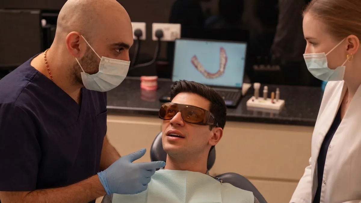 Clinician examining the face of a patient in protective glasses, with a nurse beside the chair