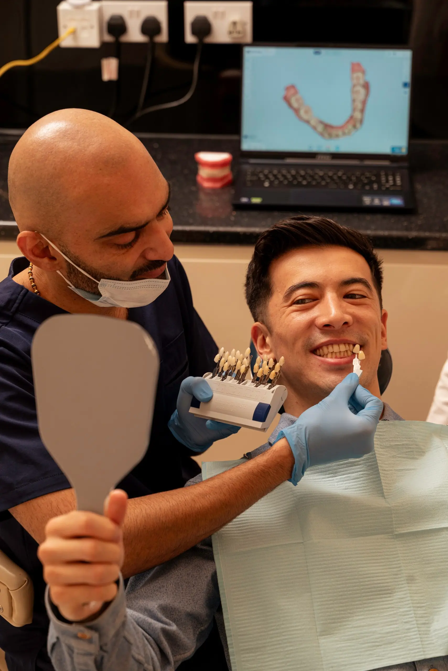 Composite fillings in Islington: dentist holding a shade guide to a smiling patient's teeth as he checks them in a mirror