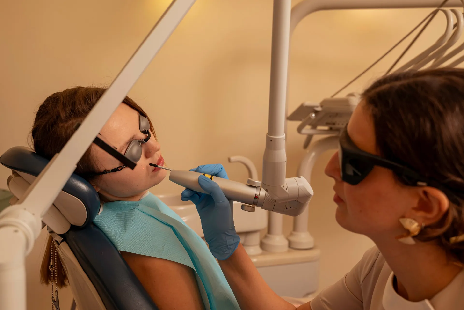 Therapist in protective glasses using a laser handpiece on a patient's face — acne treatment