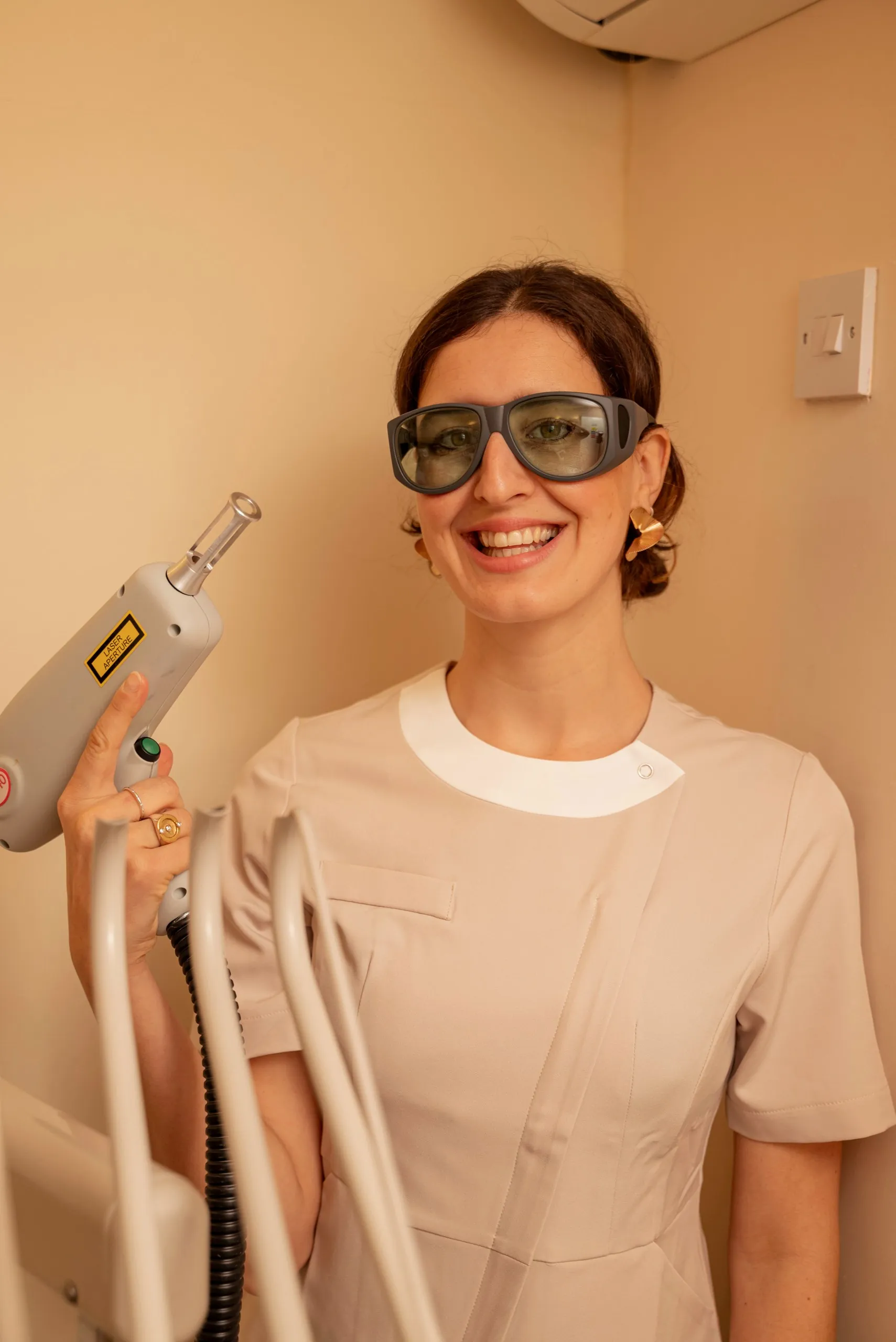 Laser body rejuvenation in Islington, London: smiling therapist in protective glasses holding a laser handpiece