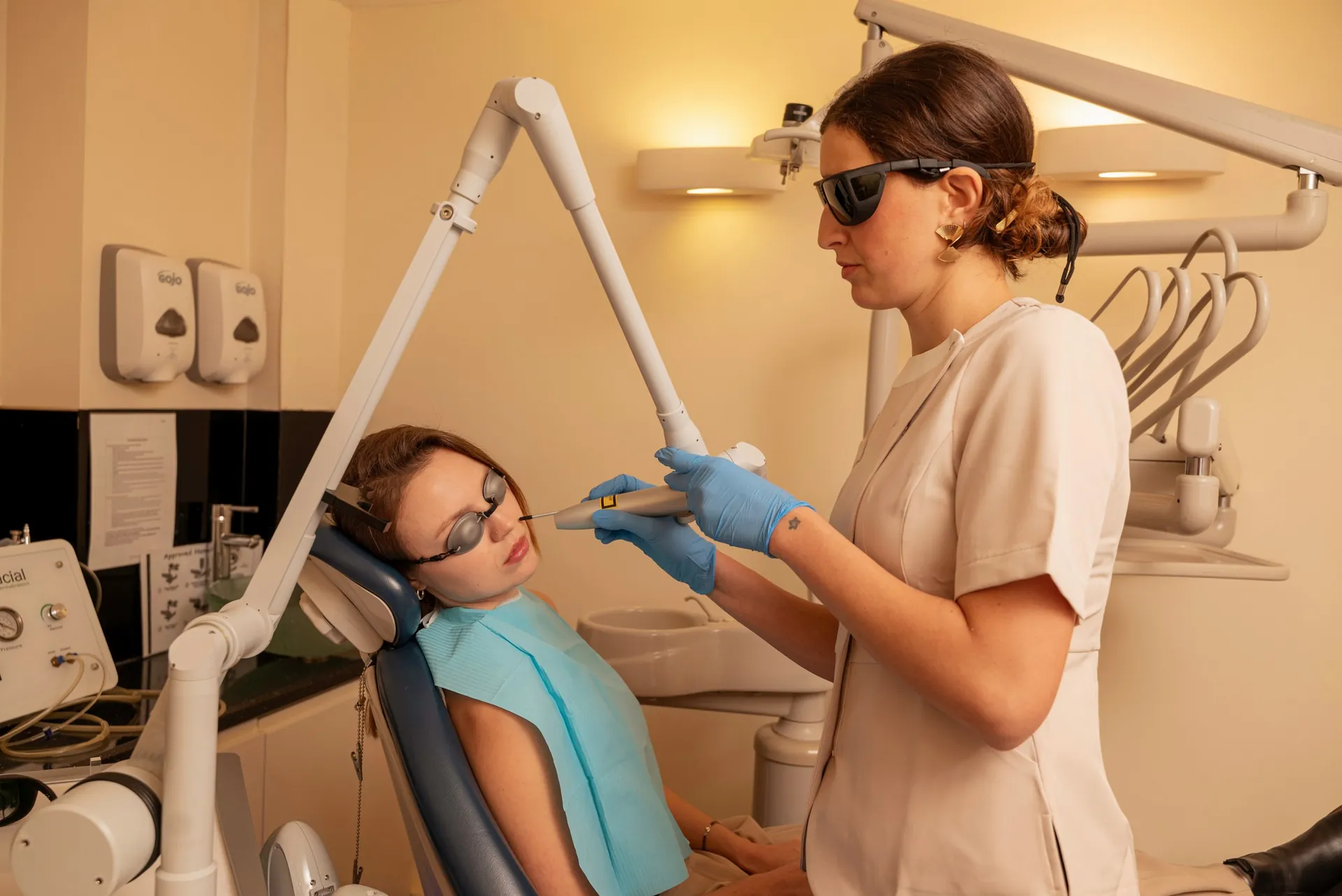 Therapist in protective glasses carrying out a laser treatment on a reclining patient's face — PicoWay alternative