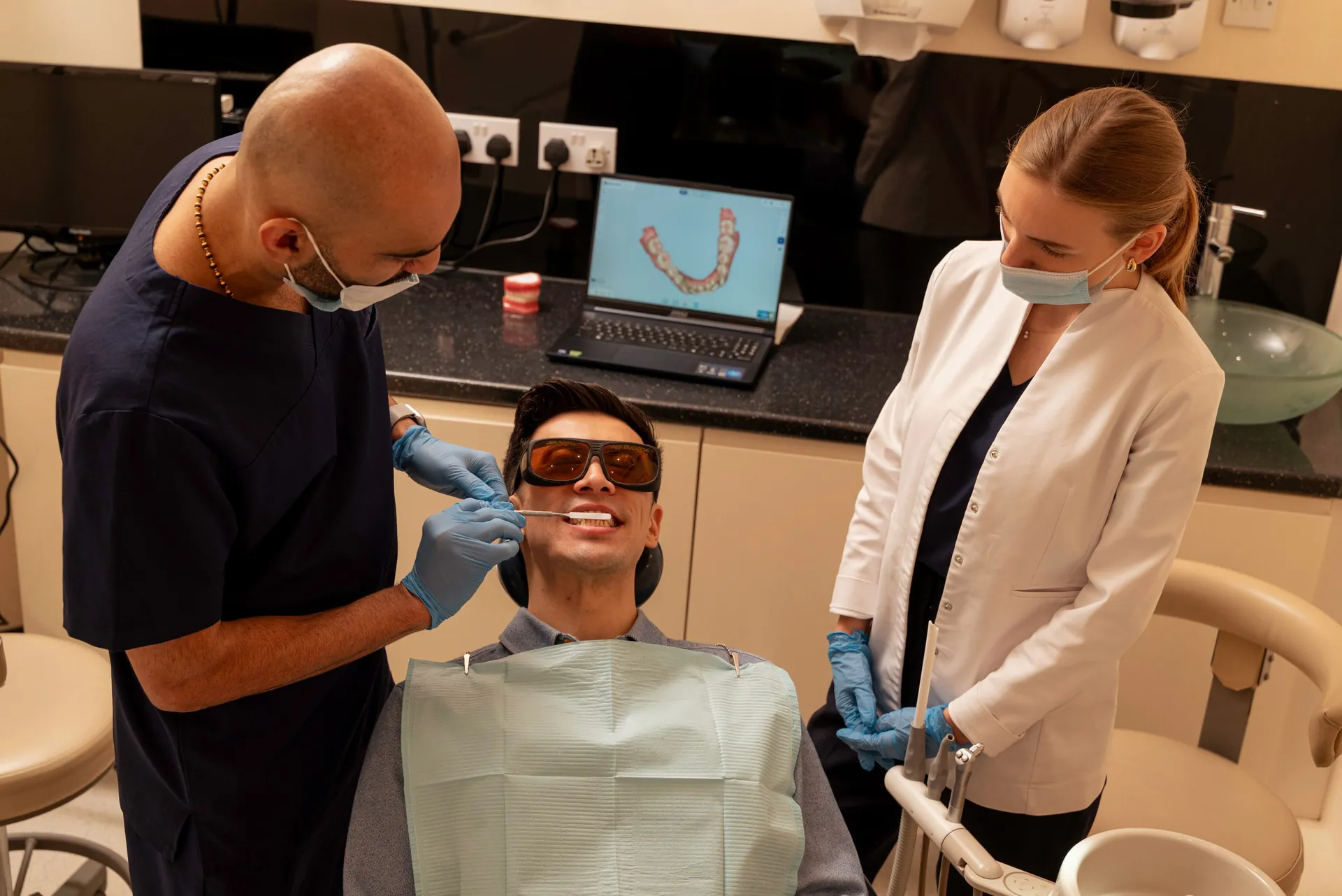 Dentist and nurse beside a patient in protective glasses, with his digital scan on a laptop