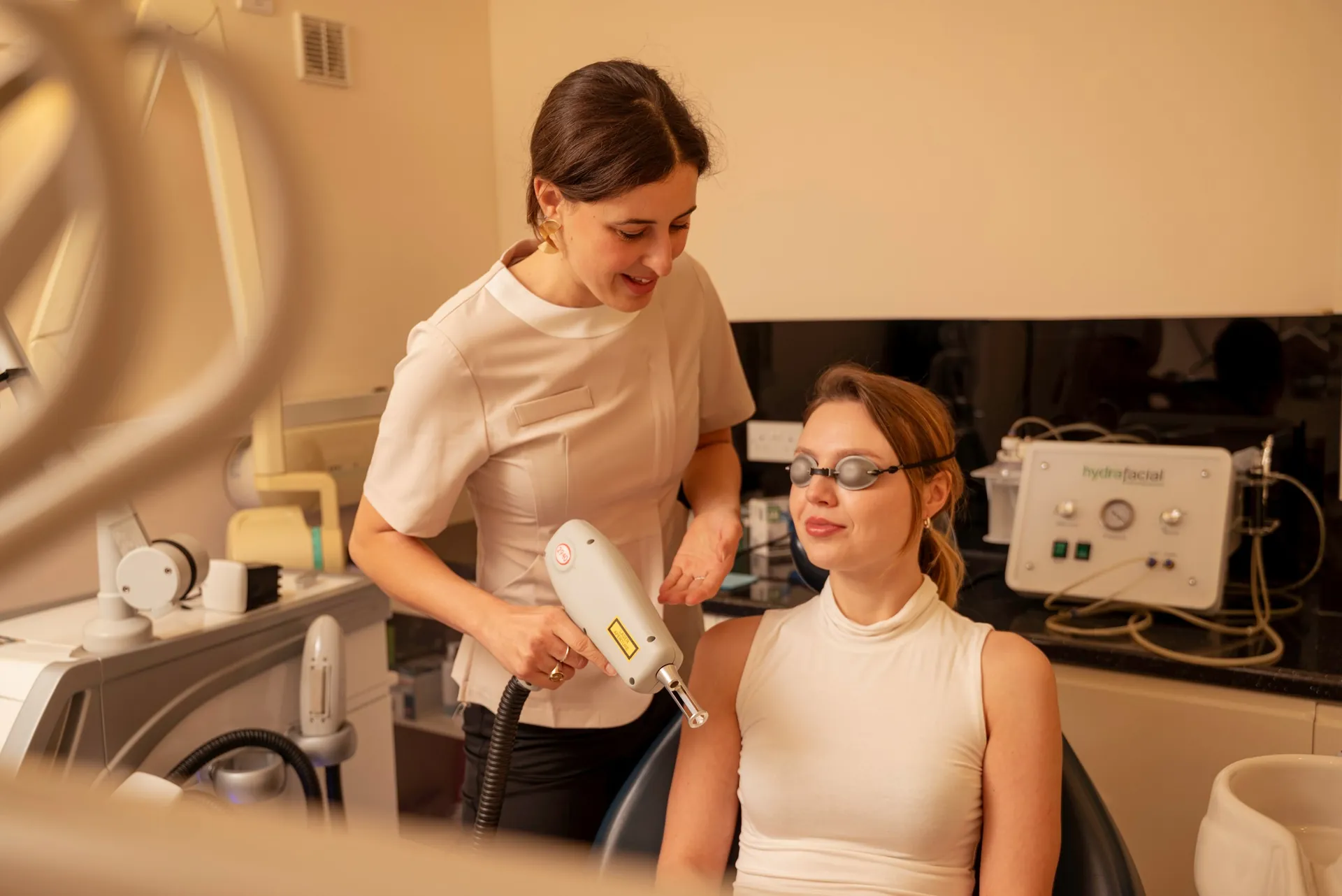 Therapist with a laser handpiece talking with a seated patient before a skin treatment