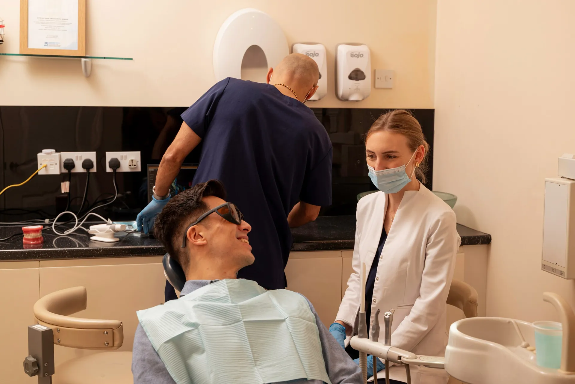 Dentist and nurse talking with a patient in protective glasses in the dental chair — chin filler