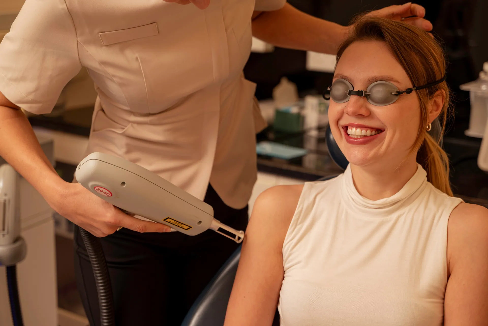 Smiling patient in protective glasses as the therapist prepares a laser handpiece
