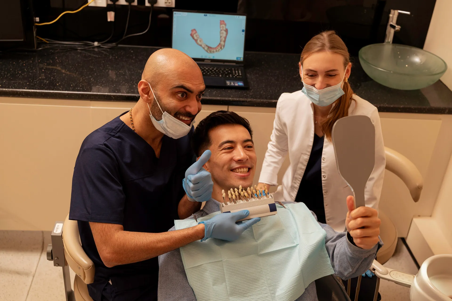 Dentist and nurse with a smiling patient holding a mirror and shade guide — composite fillings