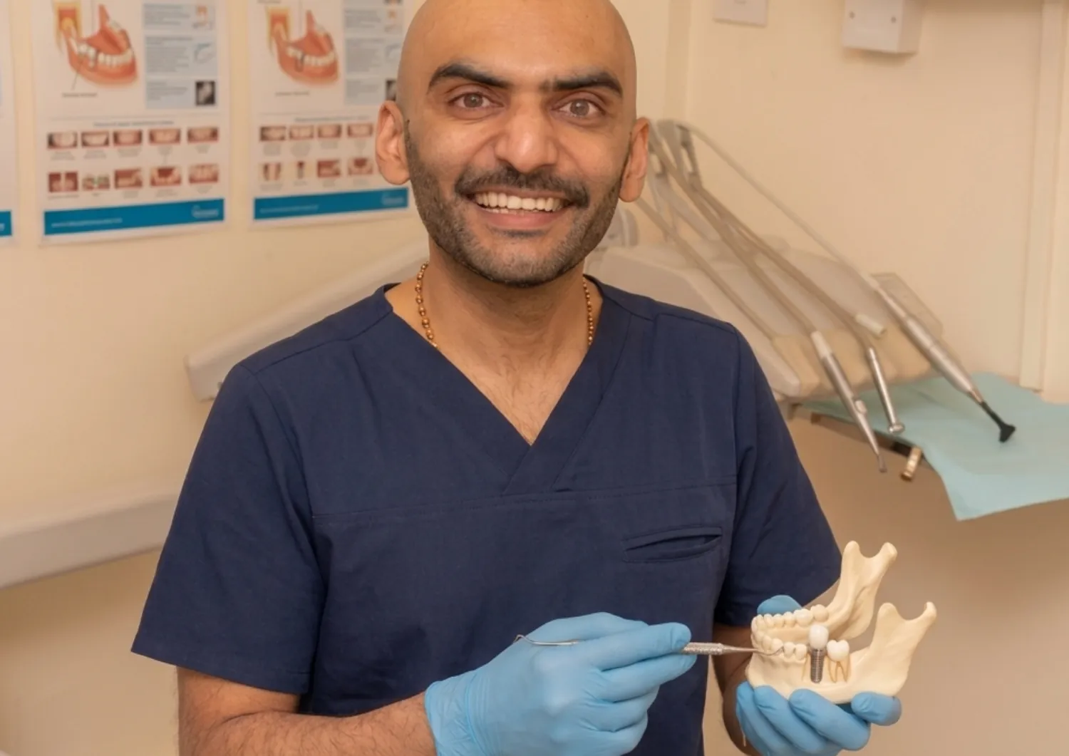 Smiling dentist holding a dental implant model in the surgery — implant bridge vs single implant