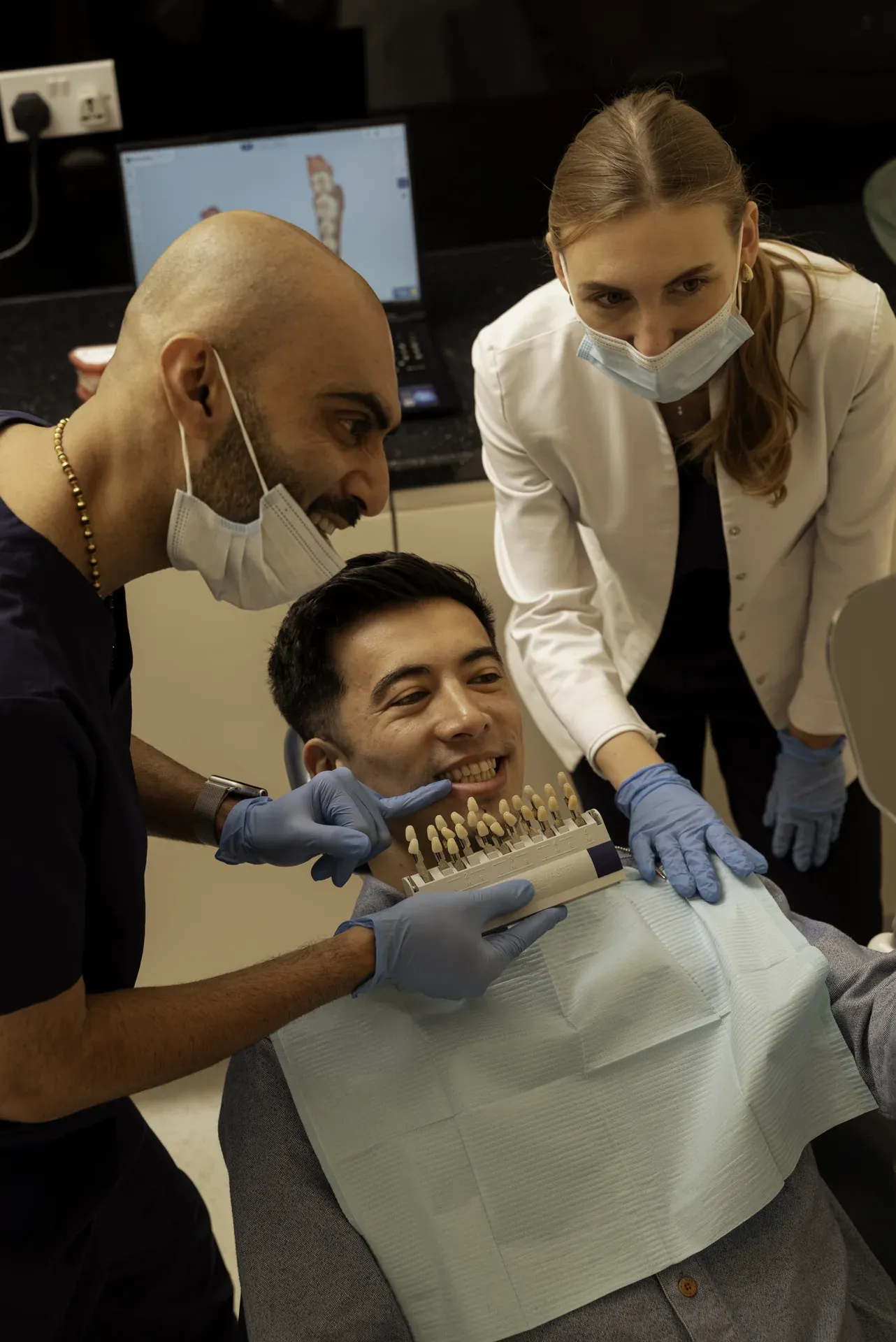 Dentist and nurse holding a shade guide to a smiling patient's teeth