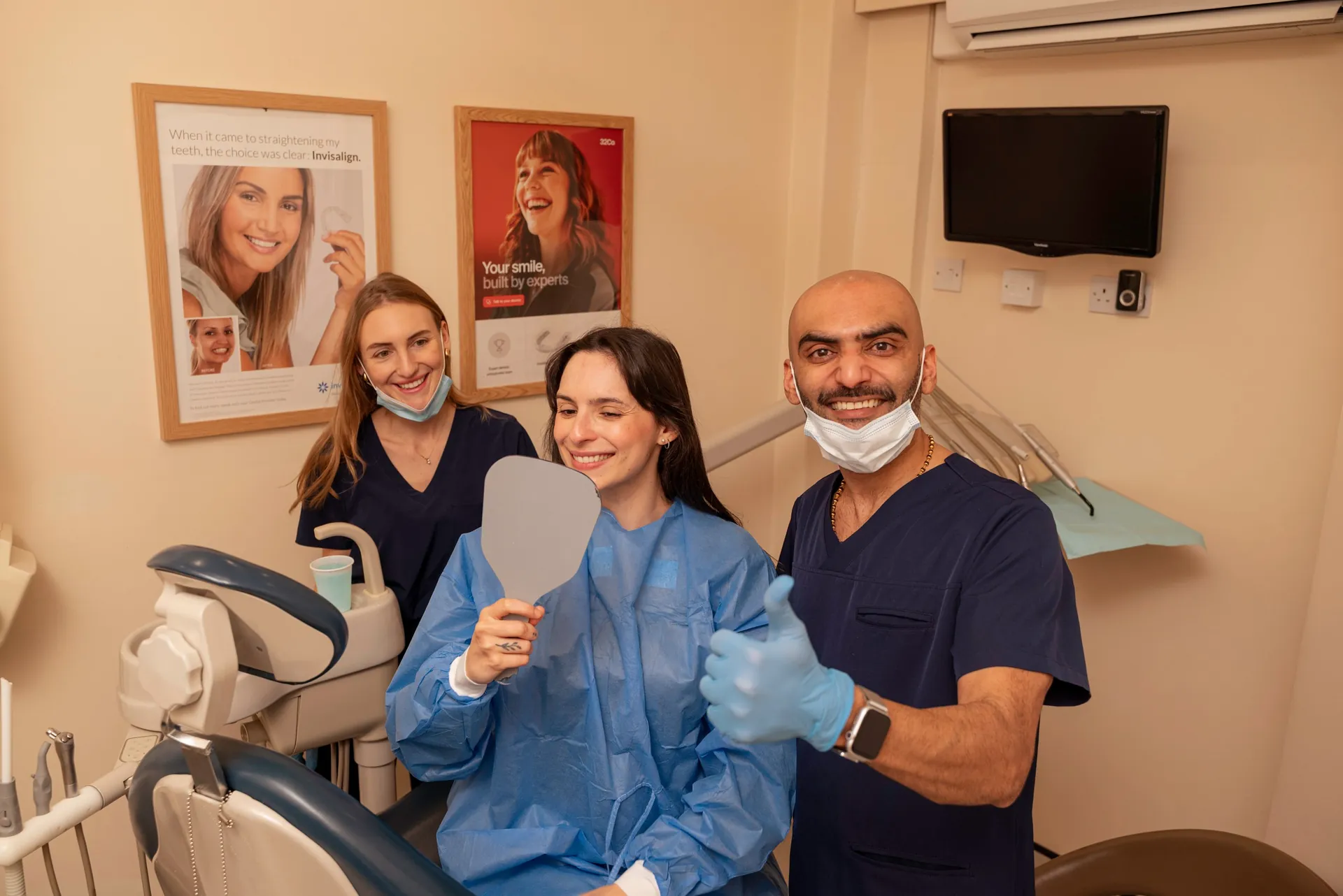 Dental team giving a thumbs up beside a smiling patient holding a mirror
