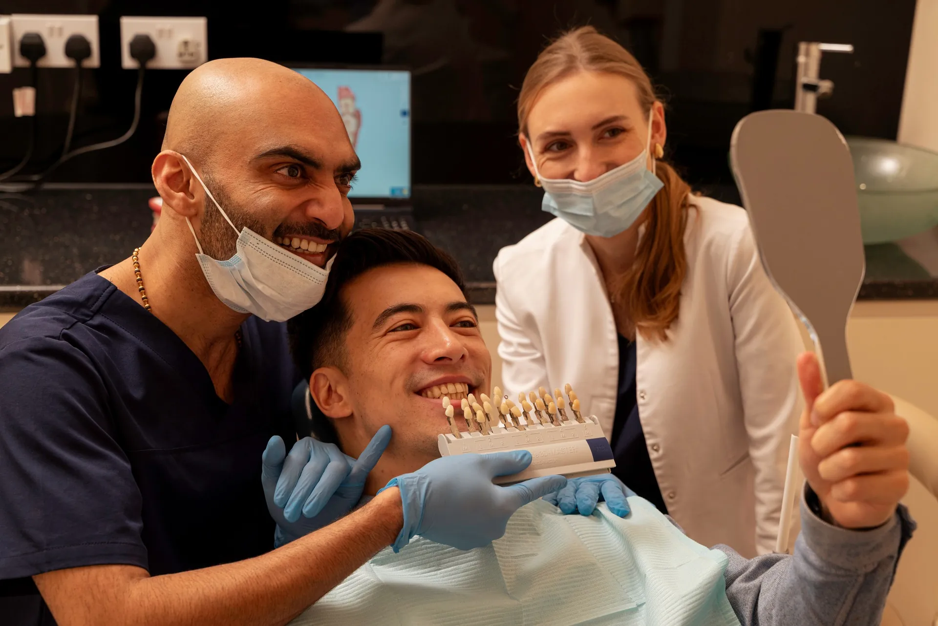 Dentist and nurse with a smiling patient holding a mirror and shade guide