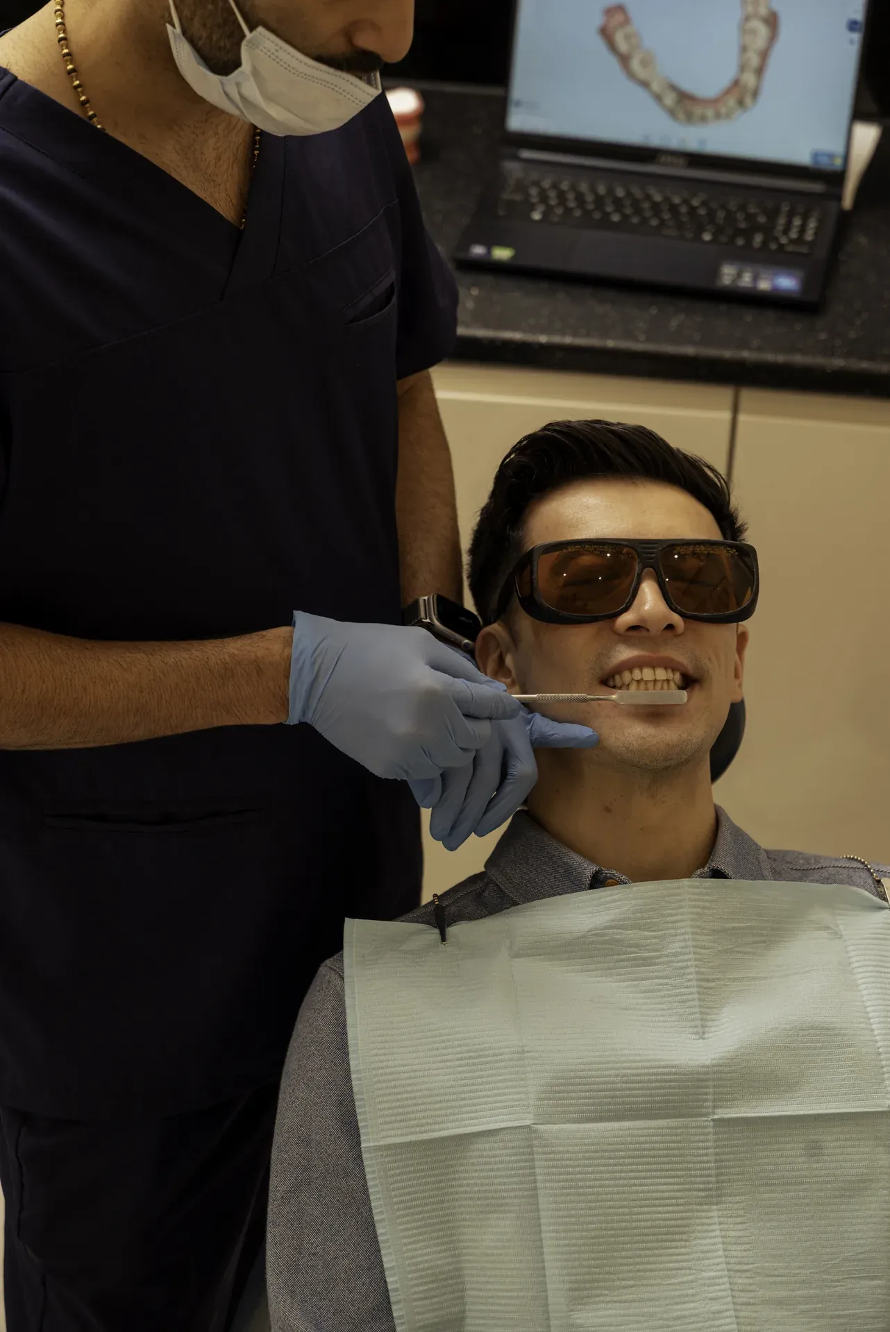 Invisalign treatment time: patient in protective glasses in the dental chair, with a digital scan of his teeth on screen