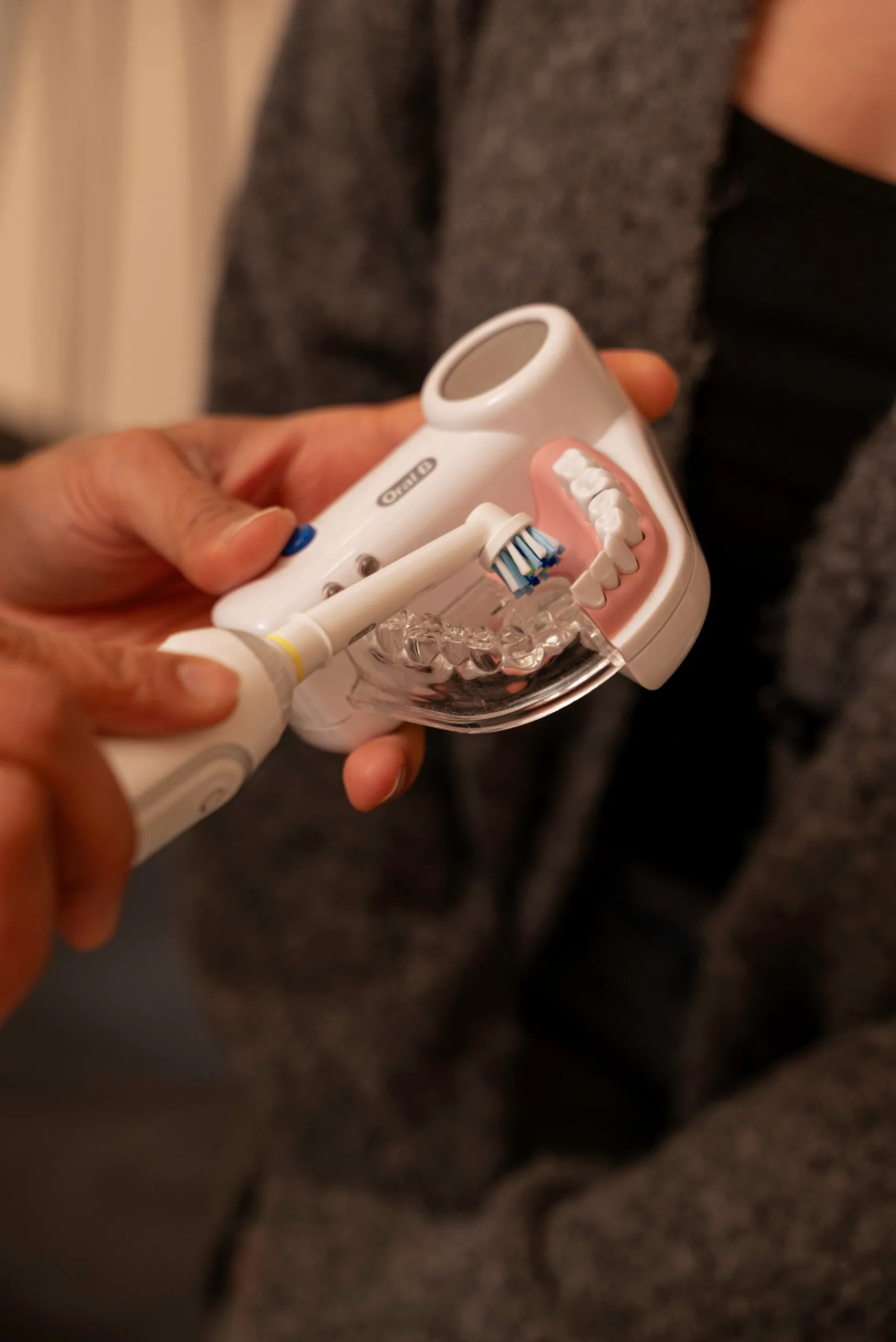 Cleaning Invisalign: hands holding an electric toothbrush beside a clear aligner
