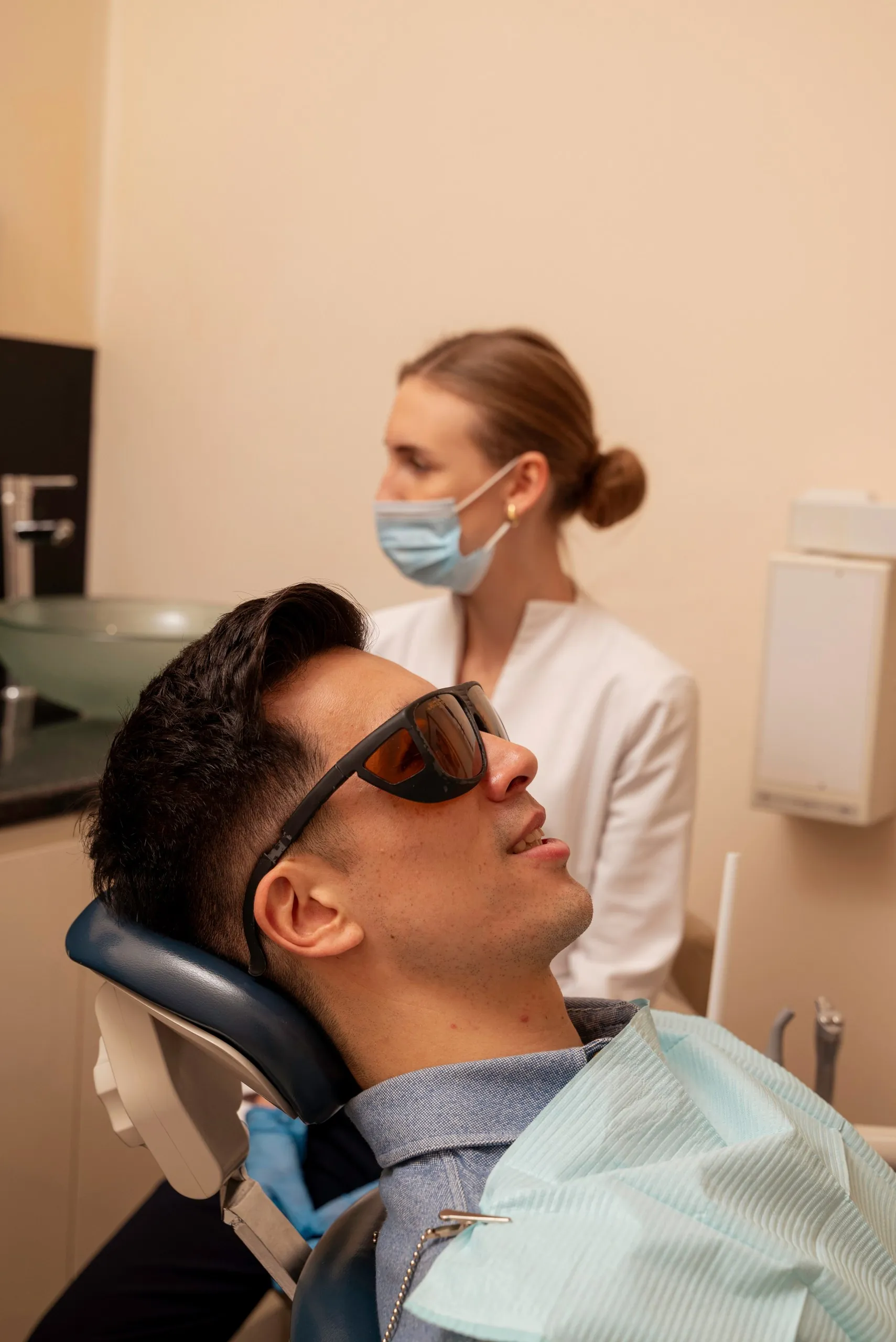 Patient in protective glasses reclining in the dental chair with a nurse behind him