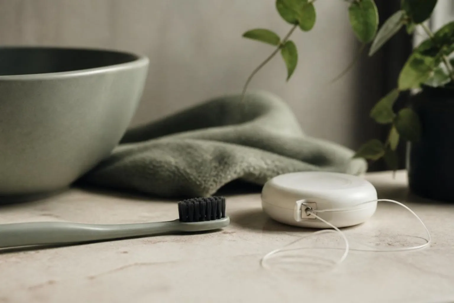A soft toothbrush and dental floss on a bathroom counter