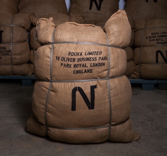 A large burlap shipping sack containing sustainably sourced raw Arabian camel hair, marked with the NOUKK brand logo.
