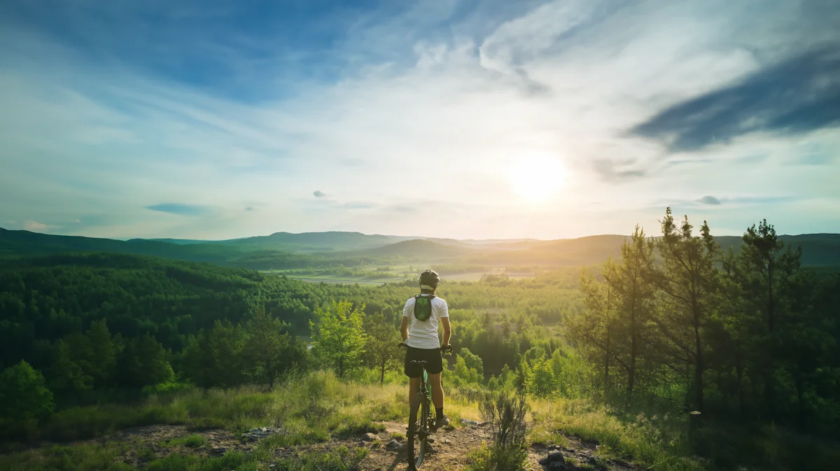 Radfahrer blickt auf eine grüne Waldlandschaft bei Sonnenuntergang.