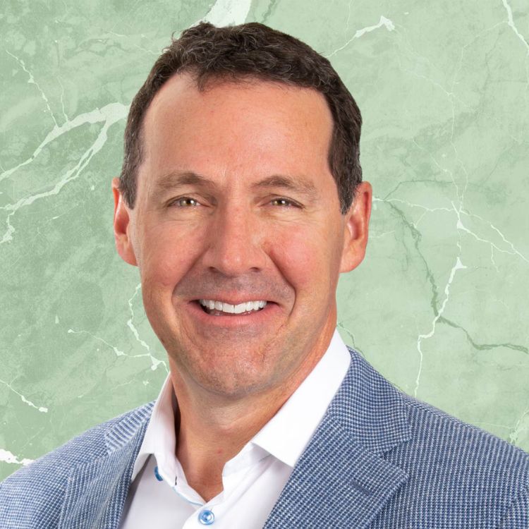 Smiling middle-aged man with short dark hair wearing a blue checkered blazer and white shirt against a green marble background.