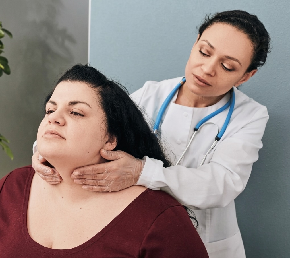 Female doctor with stethoscope examining a woman's neck in a medical office.