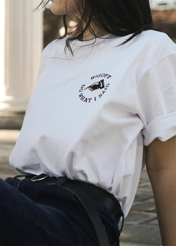 A woman is at a technology trade fair, wearing a T-shirt with a company logo printed on it, and is smiling as she looks at the design