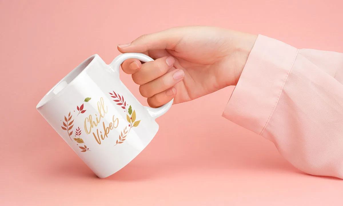 Junge Frau hält Keramiktasse mit Aufdruck in die Kamera vor rosafarbenem Studiohintergrund