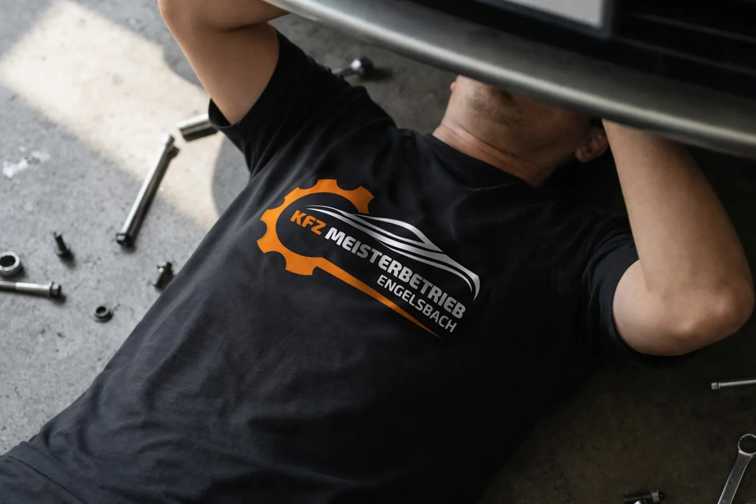 Mechaniker in schwarzem T-Shirt mit individuellem Firmenlogo eines KFZ-Meisterbetriebs