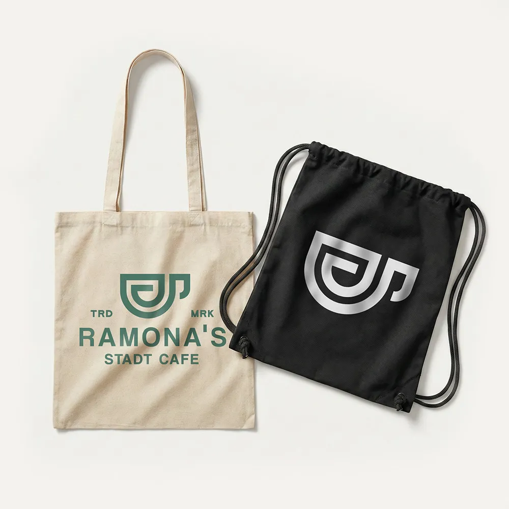 Beige Tragetasche und schwarzer Turnbeutel, beide mit dem Logo von Ramona’s Stadt Cafe.