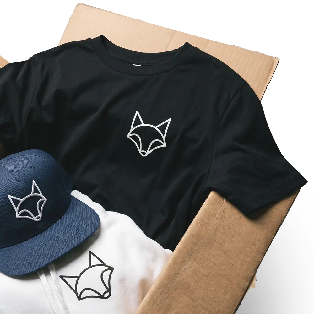 Schwarzes T-Shirt, weißer Hoodie und blaue Kappe mit einfachem Fuchslogo auf brauner Pappe.