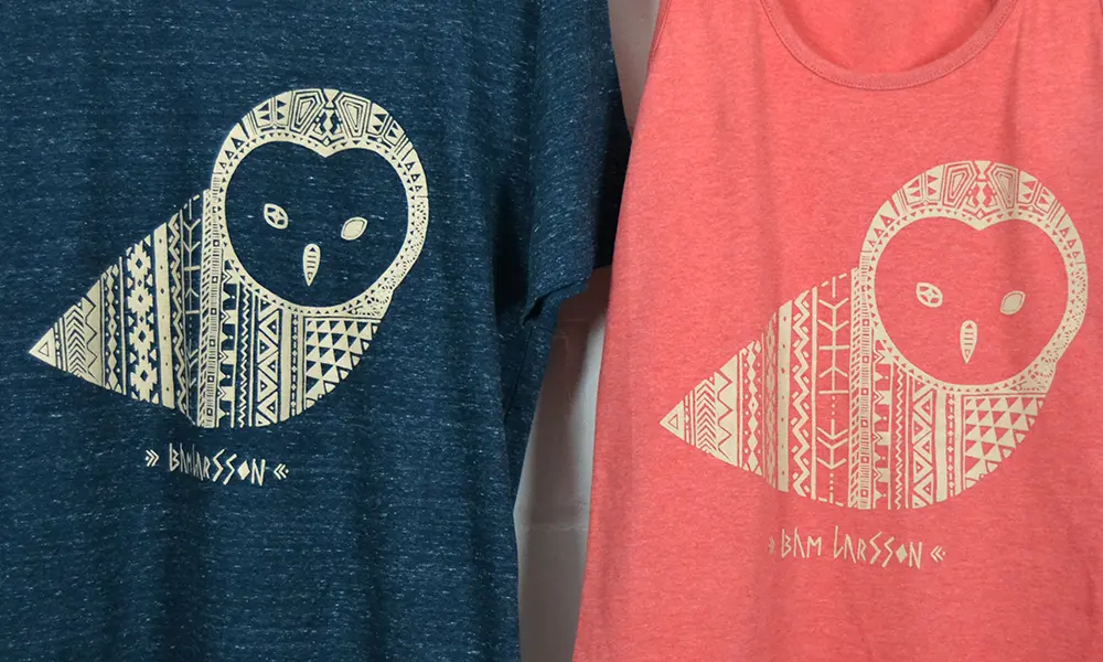 Blaues und rotes T-Shirt mit stilisierter Eulenillustration und Text ‚BAM LARSSON‘.