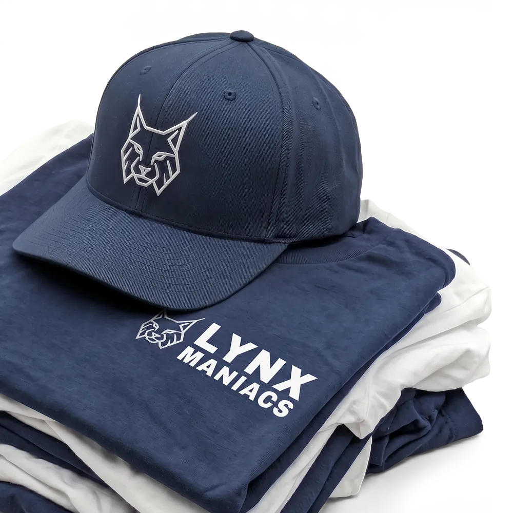Dunkelblaue Kappe mit Lynx-Logo liegt auf gefalteten T-Shirts in Blau und Weiß.