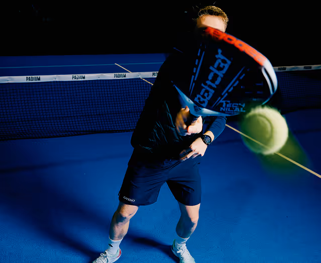 Man playing padel hitting a ball with a racket on a blue court with a net in the background.