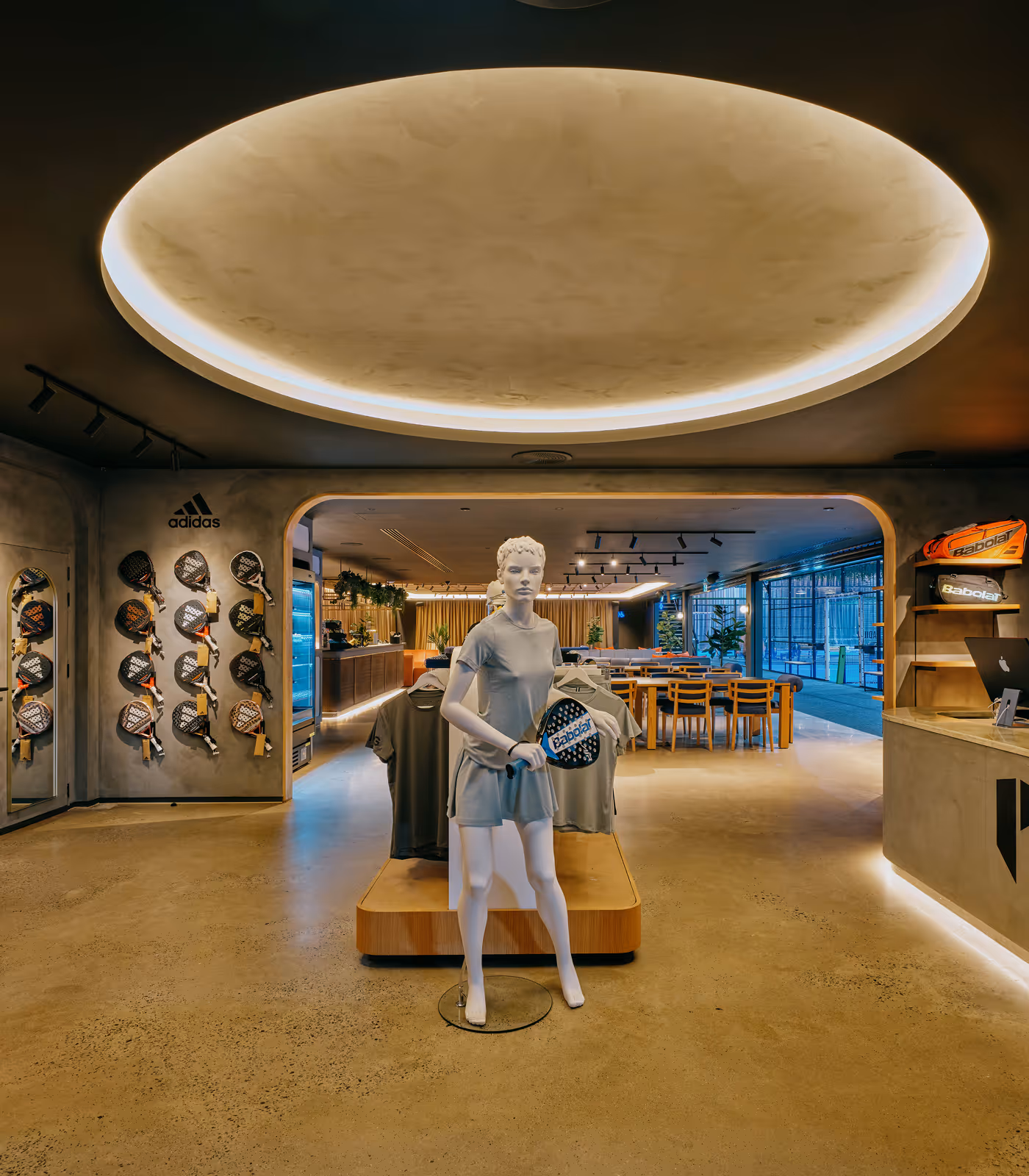 Interior of a modern sports store with a mannequin holding a paddle racket, racks of paddles on the wall, and seating area in the background.