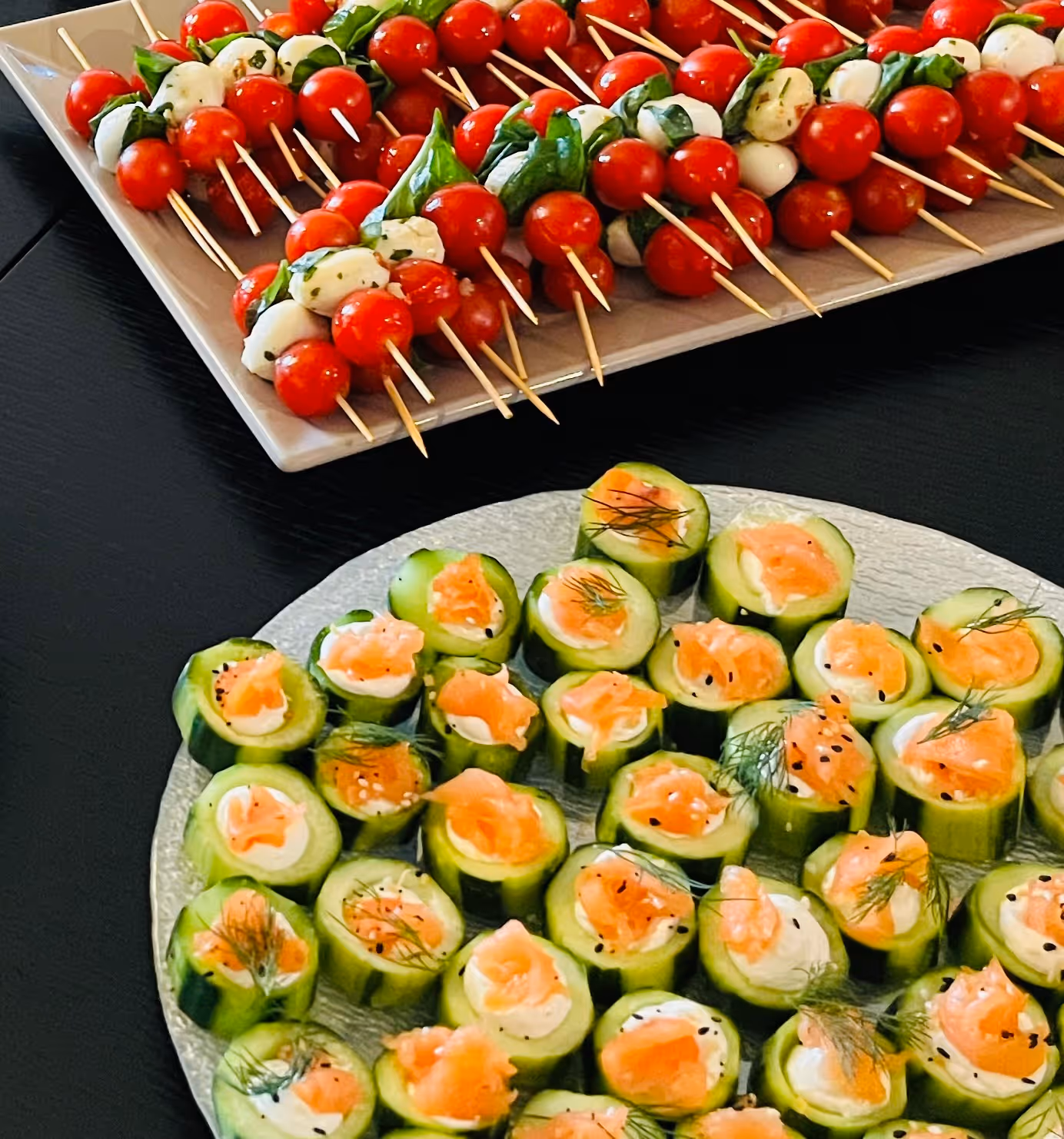 Stuffed cucumbers and mozzarella and cherry tomato skewers displayed on plates on a table
