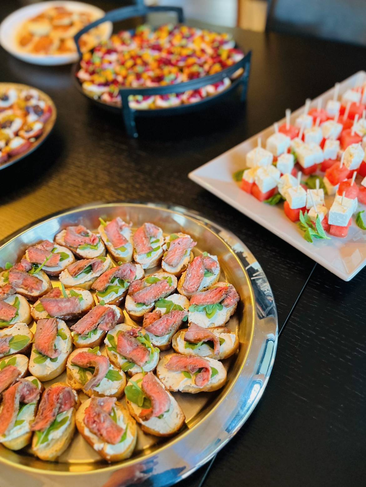 A perspective view of a long dining table elegantly styled with a variety of bespoke finger food platters for a private catered event.