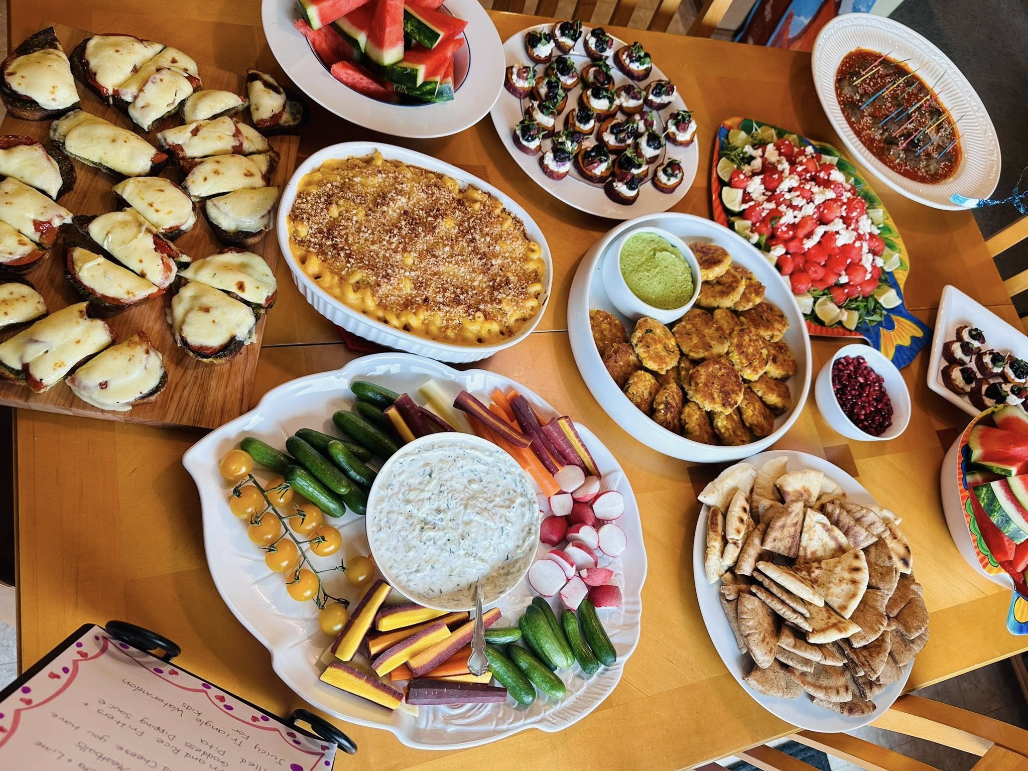 A series of rectangular wooden boards arranged with sliced meats, assorted nuts, and olives, paired with hummus, fresh pita, and seasonal roasted fruits."