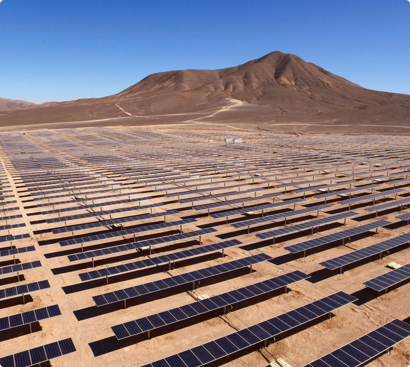 Dozens of rows of solar panels in a desert with a mountain in the background