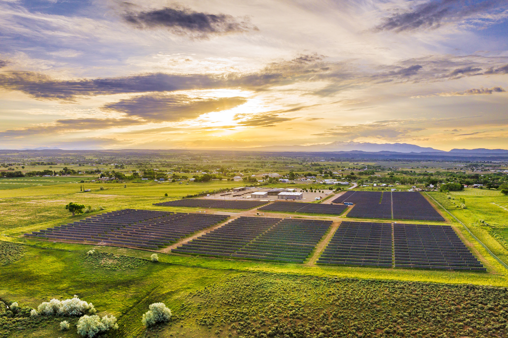 Aerial view of solar panels in a field with the sun setting in the background