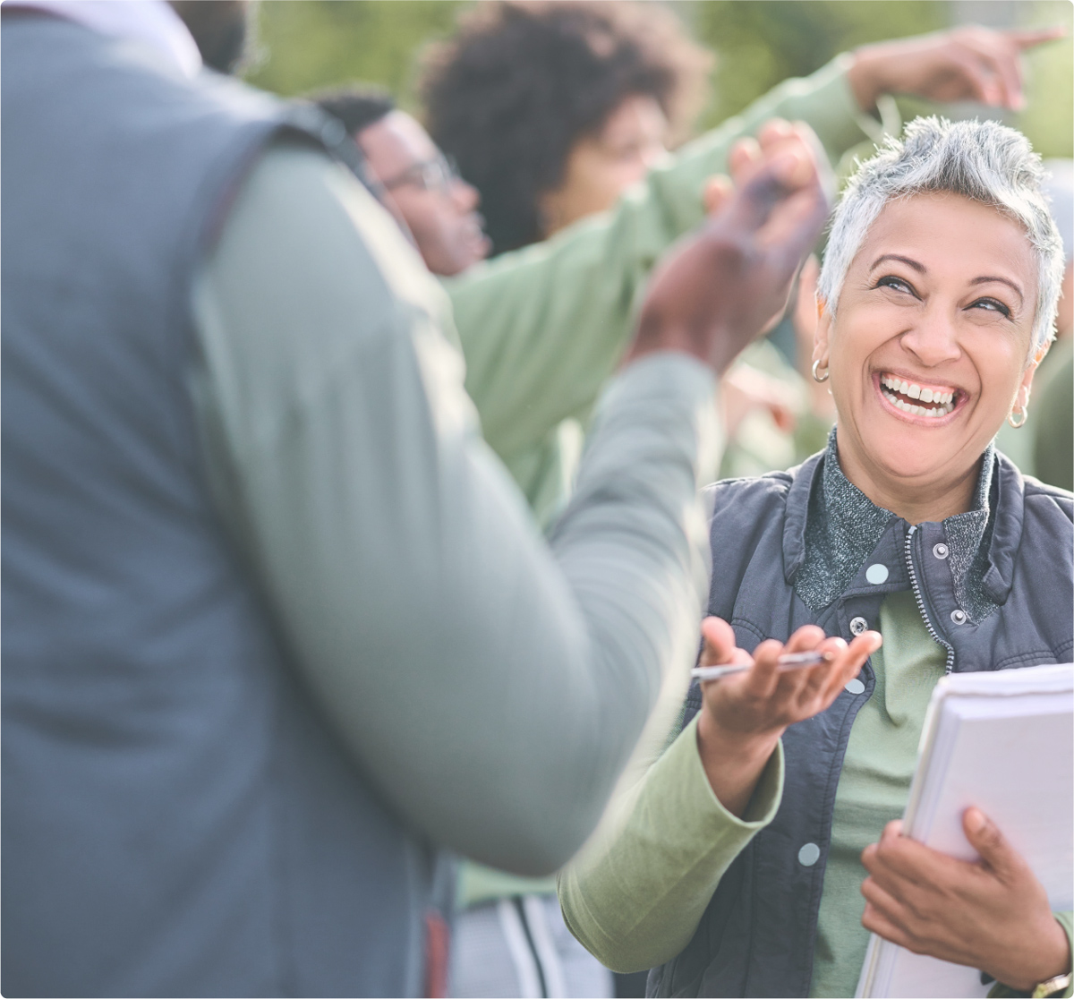 A person smiling at another person while holding a notebook and pen