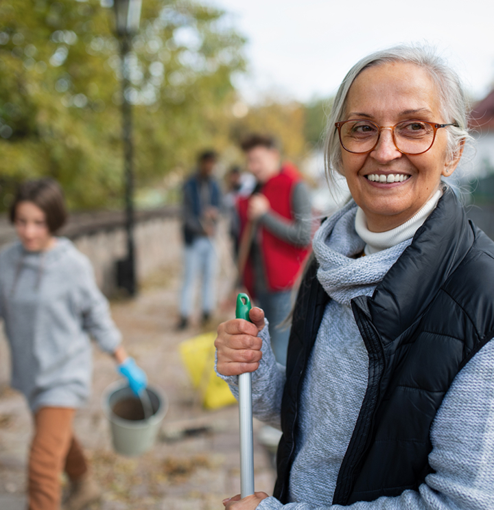 A smiling woman holding a broom and volunteering while other volunteers work in the background