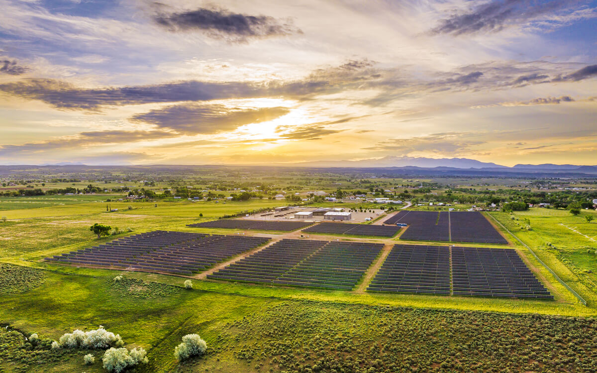 An aerial view of solar panels in a field with the sun setting in the background